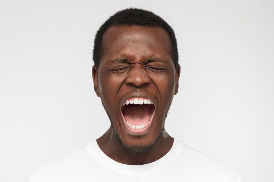 Close Up Portrait Of Screaming With Closed Eyes Crazy African American Man In Blank White T-shirt Isolated On Gray Background