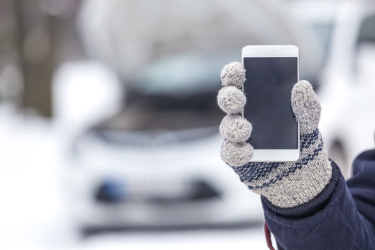 Man Holding Blank Screen Smartphone Next To Car With Opened Hood. Winter Season Road Assistance Concept.