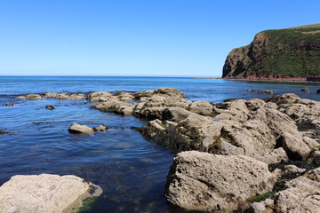 Close up of rocks by sea in foreground with sea and cliffs beyond