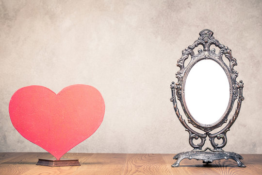 Retro old makeup mirror frame and Valentine's day love heart blank on wooden table front concrete wall background. Vintage style filtered photo