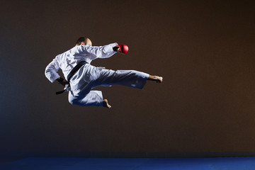 Sportsman with a black belt and red overlays on his hands beats a kick in the jump
