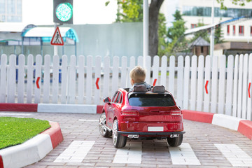 Little kid on a children's electric car is driving on special road for kids with traffic signs and...