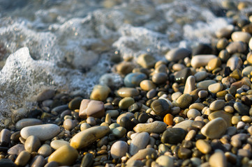 pebble stones on the sea beach, the rolling waves of the sea with foam