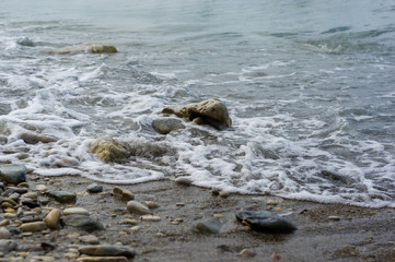 pebble stones on the sea beach, the rolling waves of the sea with foam