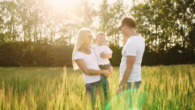 Young parents go to the field with spikelets of wheat in white T-shirts and jeans