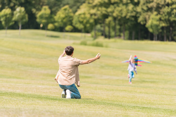 back view of father with open arms looking at little daughter playing with kite in park