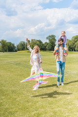 Fototapeta premium happy young parents and cute little daughter playing with colorful kite in park
