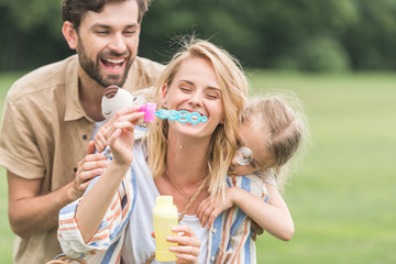 Fototapeta premium happy family with one child hugging and blowing soap bubbles in park