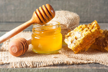 Honey dripping from a wooden honey dipper in a jar on wooden grey rustic background