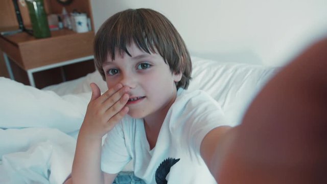 Sweet, lovely boy records a video, shows a tablet he owns to his followers. Filming in bed, little vlogger, new generation. Having fun, active lifestyle.