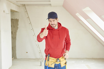 Portrait of handsome young handyman giving thumbs up while standing at construction area at the the...