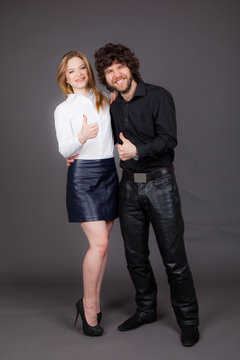 A girl in white stands next to a man in black. Both show a gesture of Laik. Studio shot