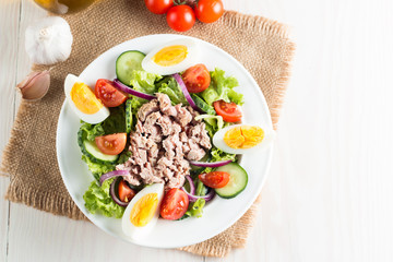 Fresh fish tuna salad made of tomato, ruccola, tuna, eggs, arugula, crackers and spices. Caesar salad in a white bowl on wooden background