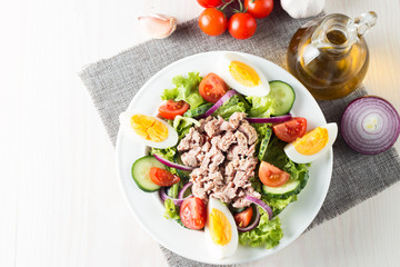 Fresh fish tuna salad made of tomato, ruccola, tuna, eggs, arugula, crackers and spices. Caesar salad in a white bowl on wooden background