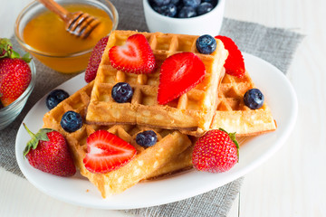 Photo of fresh homemade food made of berry Belgian waffles with honey, chocolate, strawberry, blueberry, maple syrup and cream. Healthy dessert breakfast concept with juice. 