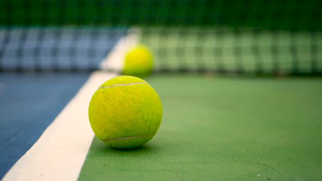 Close up of tennis equipment on the court. Sport, recreation concept. Yellow tennis balls in motion on a clay green blue court next to the white line with copy space, soft focus and net in background.