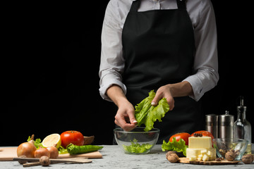The chef prepares a salad, digs up lettuce leaves, on a dark background with an empty space for an inscription
