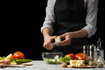 The chef prepares a salad, slicing feta cheese, mozzarella, on a dark background with an empty space for writing