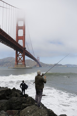 A fisherman with a fishing rod near of Hoppers Hands in Golden Gate Bridge, at Marine Drive  The Golden Gate is a famous suspension bridge connecting the city of San Francisco to Marin County.