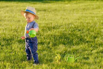 Toddler child outdoors. One year old baby boy wearing straw hat using watering can