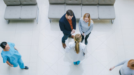 High Angle Shot in the Hospital Lobby, Young Couple Talks Meets with  Female Physician / Doctor /...