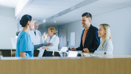 In the Hospital at the Reception Desk Nurse on Duty Answers Young Couple Patients and Showing Them a Way.