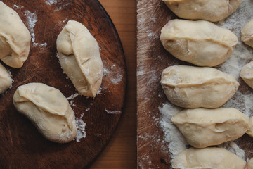 Stuffed vareniki or dumplings on brown board dusted with flour. They may be stuffed with cherry, potato or cabbage. This is a traditional Ukrainian and Russian dish.