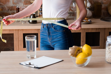 lemon and ginger detox diet for weight loss. slim and fit body. woman measuring her waist with a...