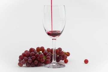 Red wine poured into a wine glass with fresh grapes. Isolated photo.