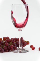 Red wine poured into a wine glass with fresh grapes. Isolated photo.