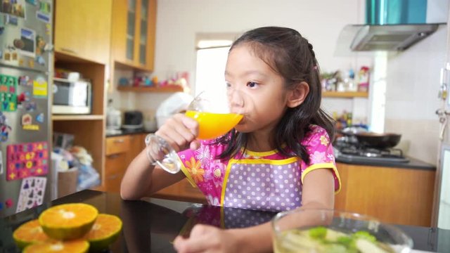 Little asian girl drinking orange juice in kitchen, slow motion footage