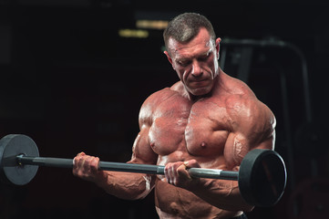 Portrait of Mature fitness model lifting barbell in gym. Strong muscular bodybuilder with naked...