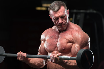 Close-up - Mature fitness model lifting barbell in gym. Strong muscular bodybuilder with naked...