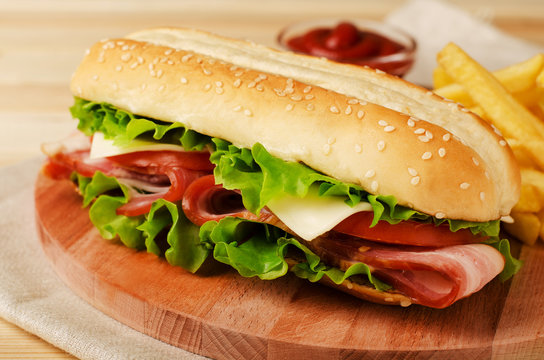 Fresh submarine sandwich with ham, cheese, bacon, tomatoes and  lettuce on wooden cutting board