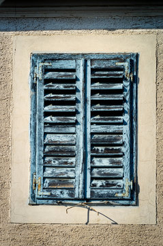 Abgenutzte Fensterlade in himmelblau an einem Haus mit einer Sandfarbenen Wand