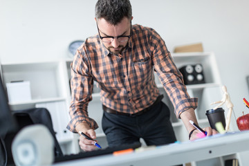 A man in the office is standing near the table and draws a marker on the magnetic board.