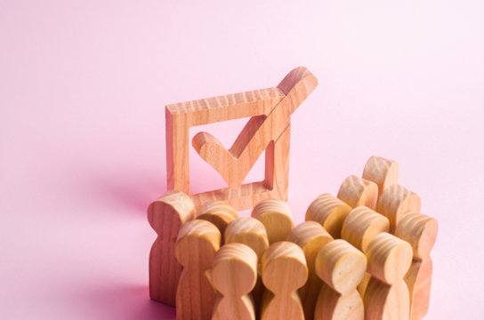 A group of wooden figures of people surround and look at a tick in the box. Voters take part in elections. Voting, referendum, social survey. Statistical data. Democratic process, institutions.