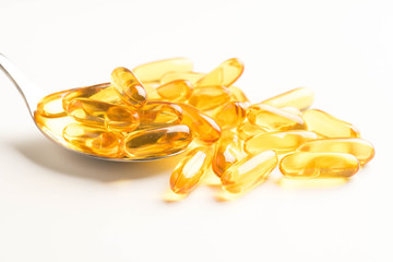 fish oil capsules in a spoon on white