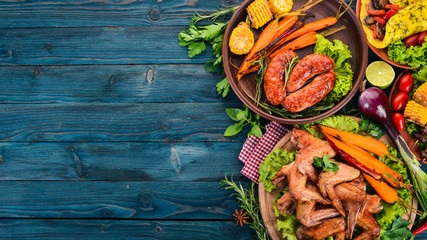 Obraz na płótnie Canvas Food. Grill sausages and chicken wings with vegetables. On a wooden background. Top view. Copy space.