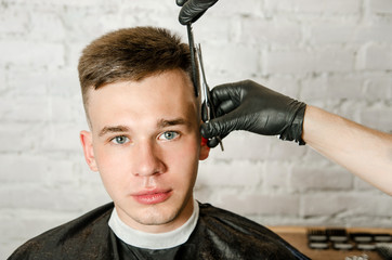 Barber does hair cut young guy on a brick wall background.