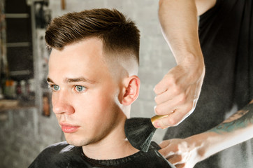The hairdresser cleans the neck of a young guy with a brush with talc after a haircut against a...