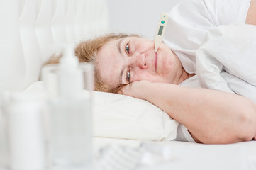 Sick senior woman with thermometer in mouth lying on the bed