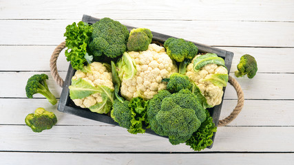 Cauliflower and broccoli in a wooden box. Fresh vegetables. On a wooden background. Top view. Copy...