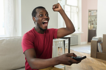 Horizontal photo of African American man dressed in bright red T-shirt watching sport match on...