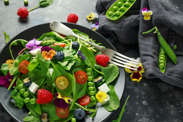 Summer salad with edible flowers, spinach, blueberries, raspberry, sweet peas, cherry tomatos and feta cheese