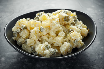 Warm potato salad with gherkins in a black plate