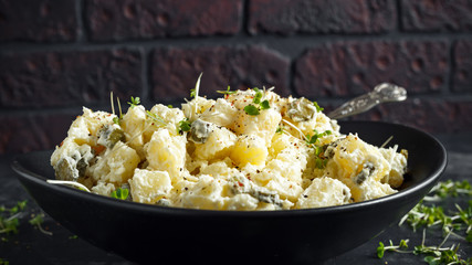 Warm potato salad with gherkins in a black plate