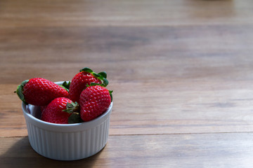 Heap fresh strawberries in the white porcelain bowl on the rustic wood table
