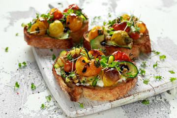 Healthy toasts with baked sweet cherry tomatoes and grilled zucchinin ribbons drizzled with...