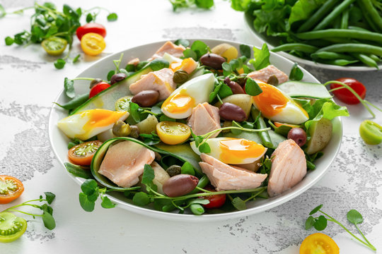 Healthy Nicoise salad with salmon, colourful sweet cherry tomatoes, olives, green beans, cucumber ribbons, soft boiled eggs, water-cress leaves with Mediterranean seasoning